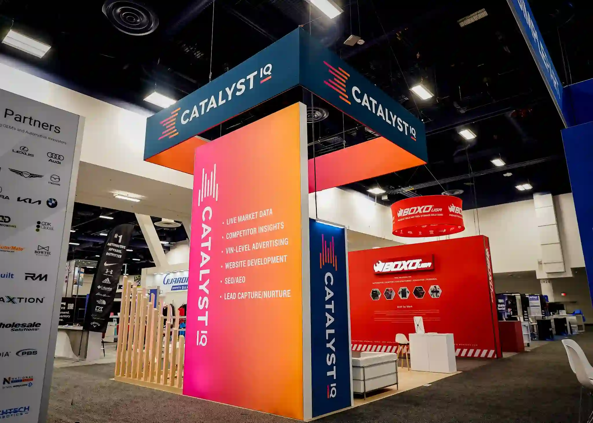Catalyst IQ booth showing vibrant gradient column listing core services: Live Market Data, Competitor Insights, VIN-Level Advertising, Website Development, SEO/AEO, and Lead Capture/Nurture