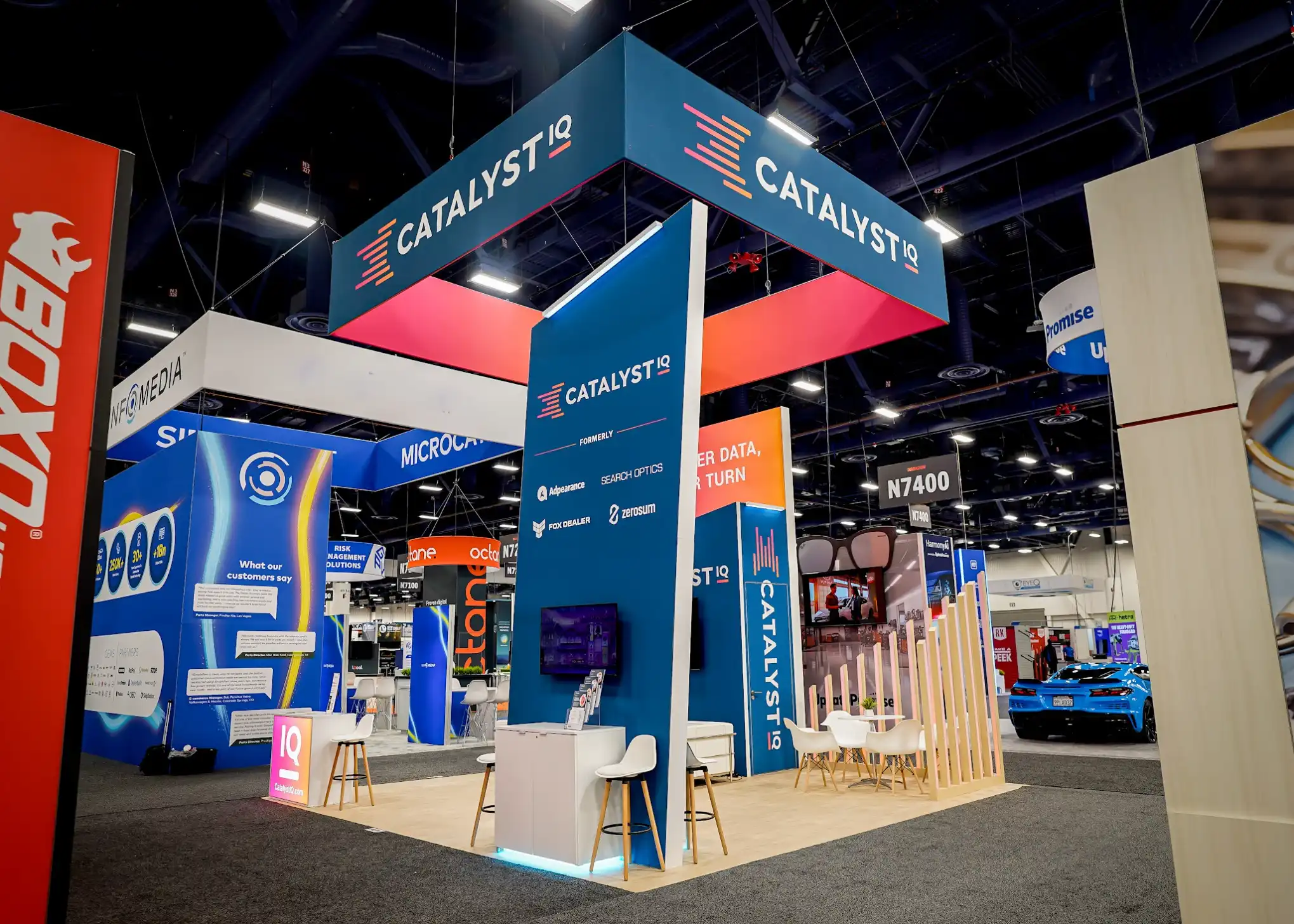 Rear view of Catalyst IQ booth showing Formerly partner logos for Adpearance, Search Optics, Fox Dealer, and ZeroSum alongside consultation stations and wood slat dividers