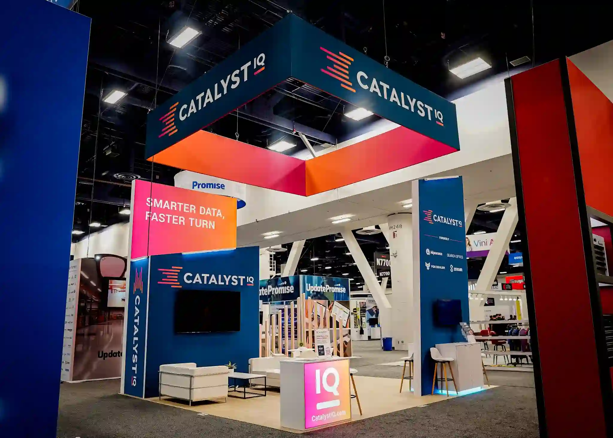 Catalyst IQ overhead hanging sign structure in teal and orange above the island booth, anchoring the new brand identity over the show floor at NADA 2026