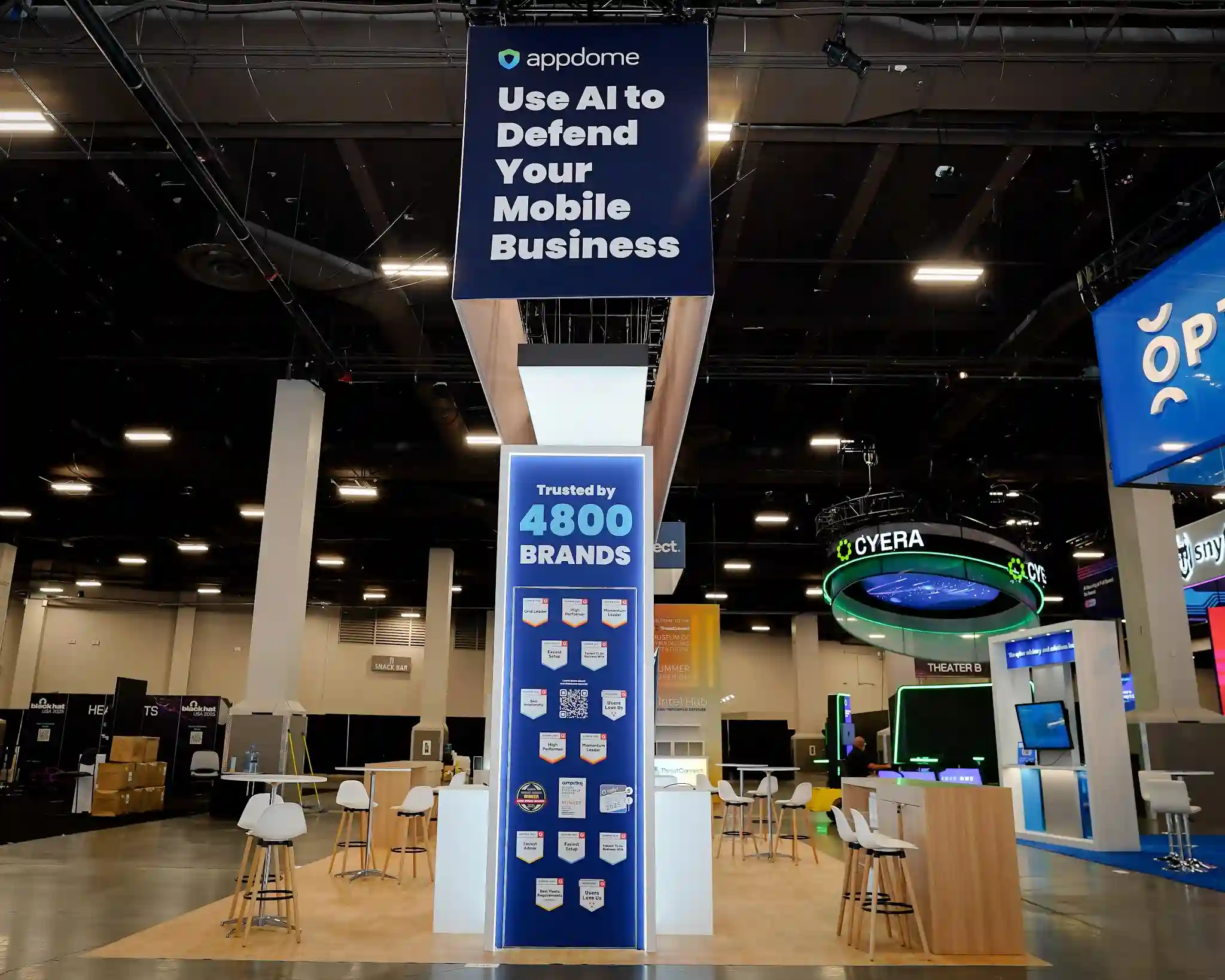 Dramatic vertical close-up looking up at Appdome hanging dark navy sign reading Use AI to Defend Your Mobile Business in bold white type, tall Trusted by 4800 BRANDS social proof column with dense grid of G2 award badges including Grid Leader High Performer Momentum Leader Easiest Setup Easiest to Do Business With and QR code for live reviews, BLACK HAT event signage visible in background, white overhead canopy with illuminated appdome shield logo above at Booth 4746 Black Hat USA 2025