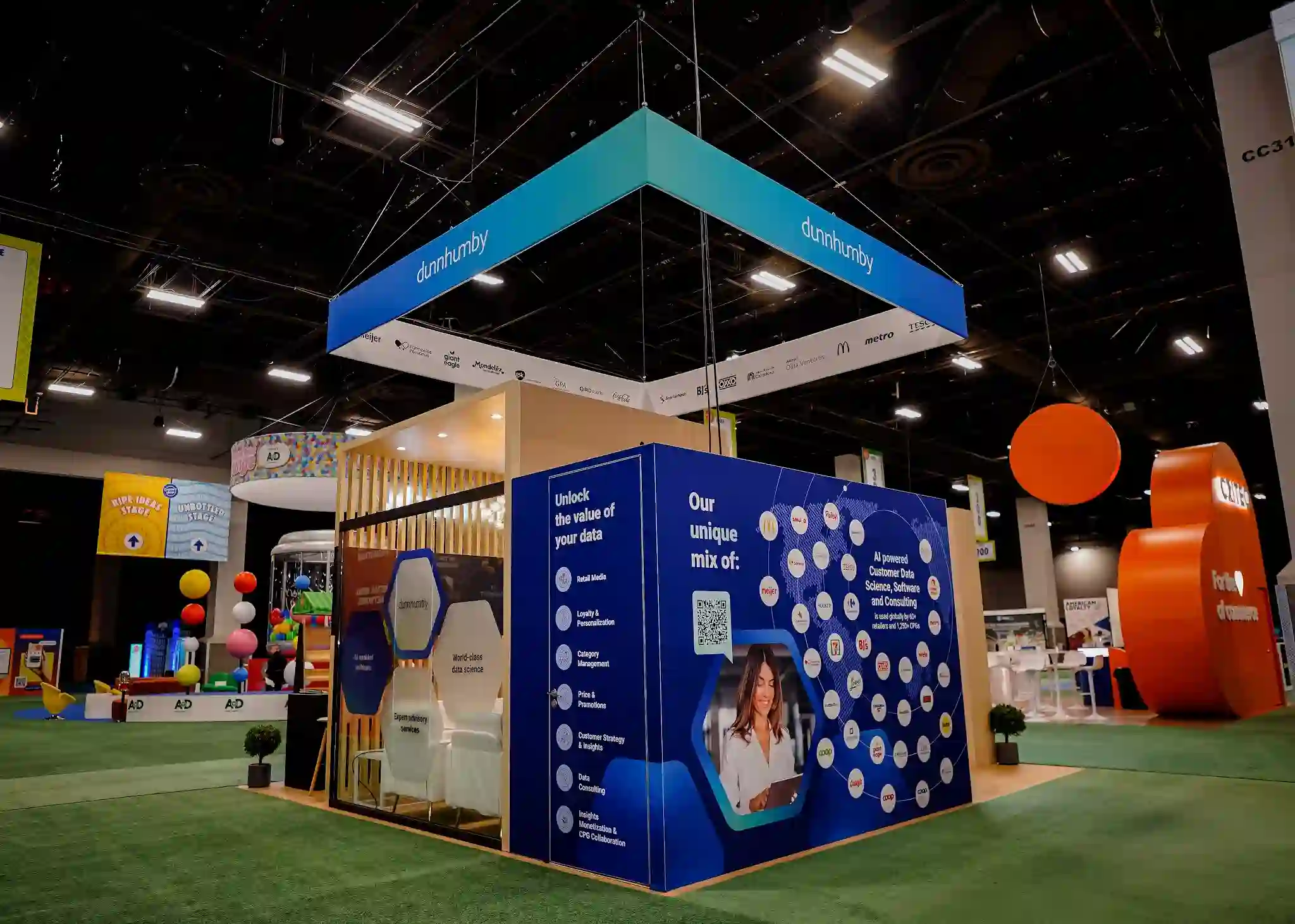 Close-up of exterior graphic panel with Unlock the Value of Your Data messaging, service list including Retail Media and Loyalty, QR code, and professional woman using tablet