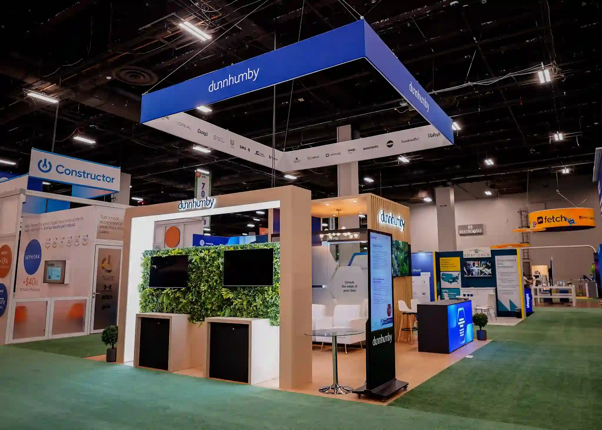 Living wall and digital kiosk area with glass-topped high-top tables, bar stools, and retail-like lighting ambiance