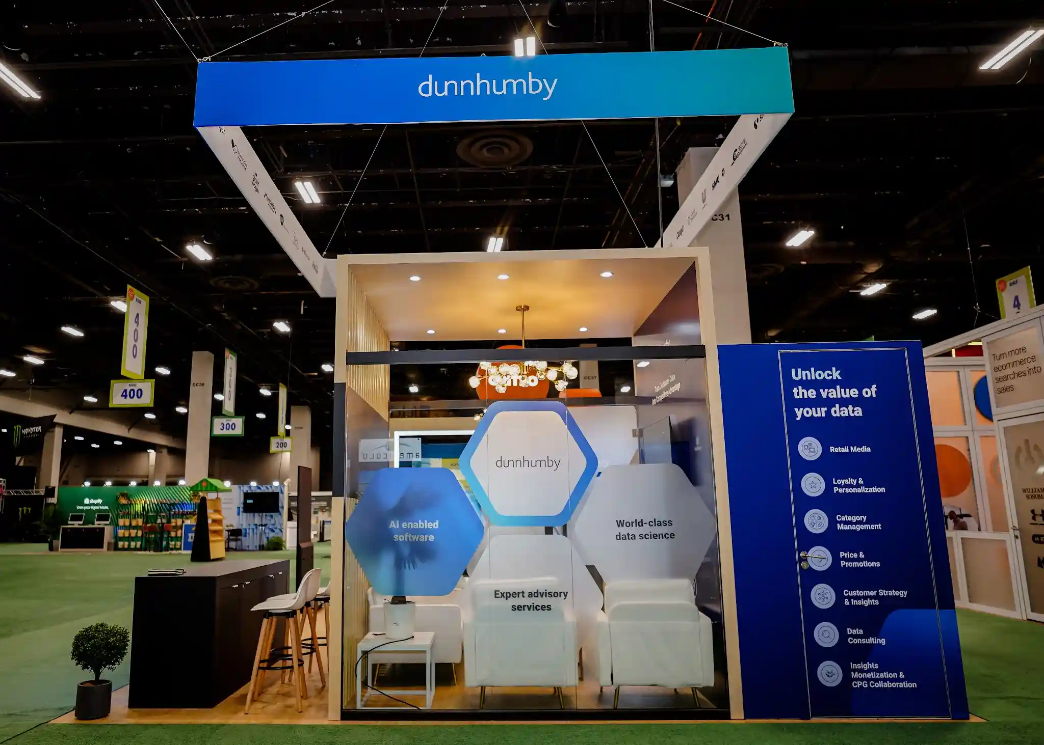 Internal meeting lounge with globe pendant Edison bulb lights, hexagonal graphic wall with AI enabled software text, white bucket chairs, and consultation table