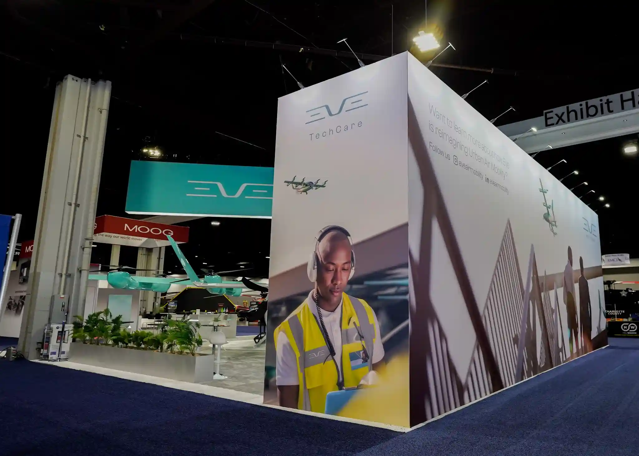 EVE TechCare corner booth with large photographic wrap showing maintenance personnel in yellow safety vest with headset, cable-stayed bridge architecture, and white corner pillar with TechCare branding