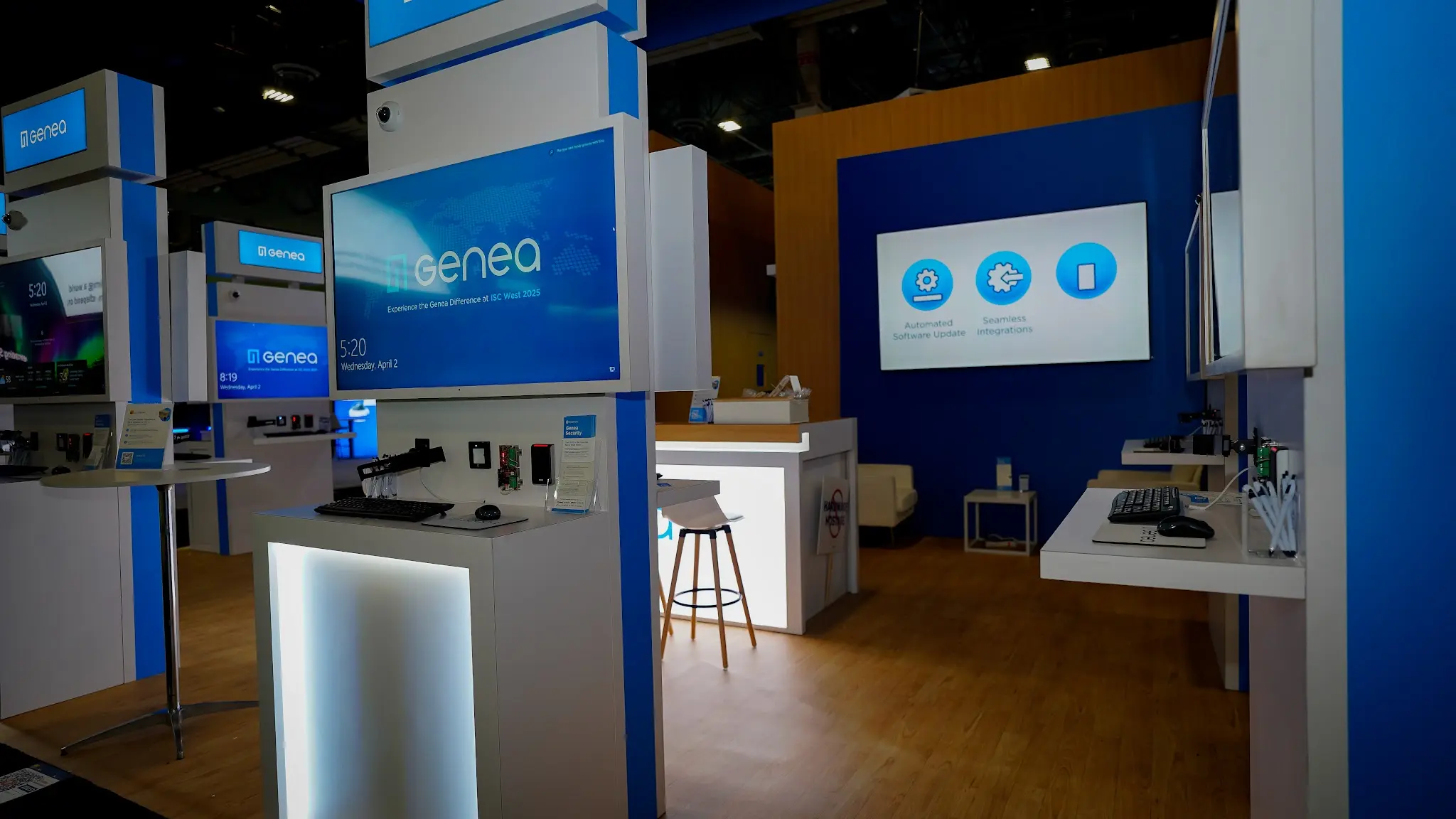 Close-up of interaction points with Automated Software Update and Seamless Integrations wall icons, demo kiosk with keyboard tray, Experience the Genea Difference at ISC West 2025 screen, and mounted security hardware