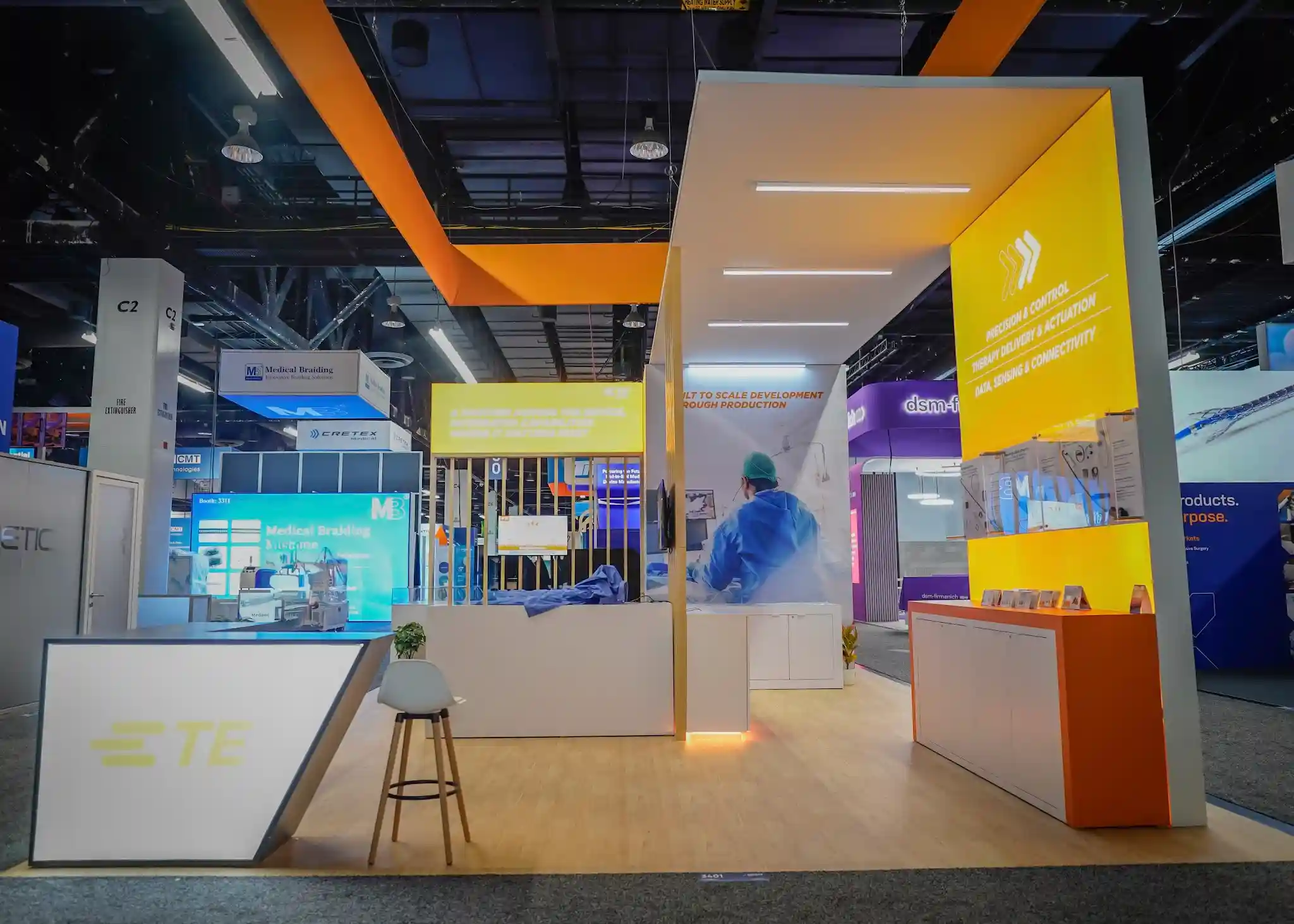 Bright yellow service portfolio wall listing Precision and Control, Therapy Delivery and Actuation, Data Sensing and Connectivity, with overhead LED bars and warm base glow