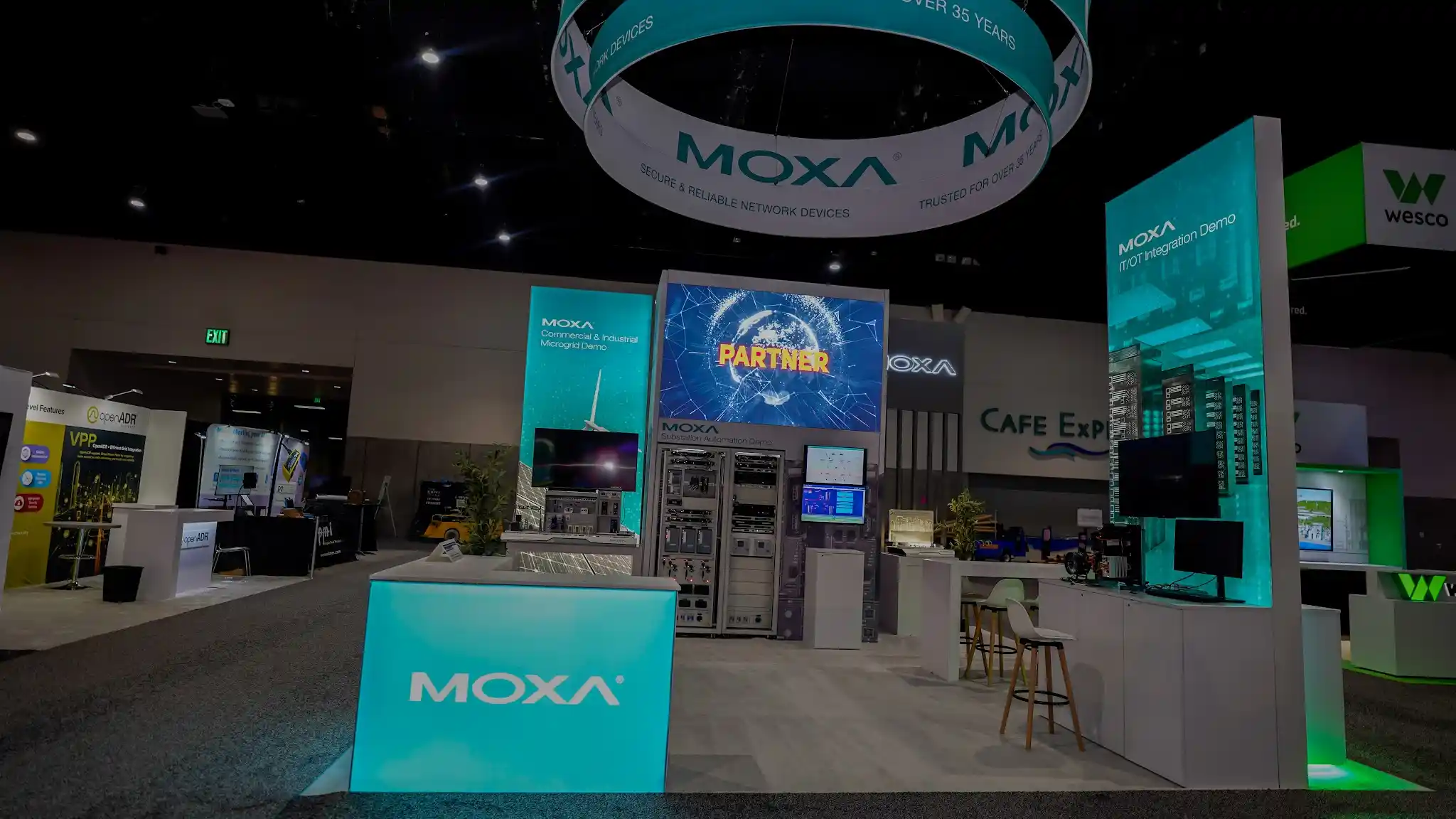 Large LED video wall displaying Partner globe graphic behind teal-lit reception counter with backlit Moxa logo, industrial controller display rack visible, and green accent pillars