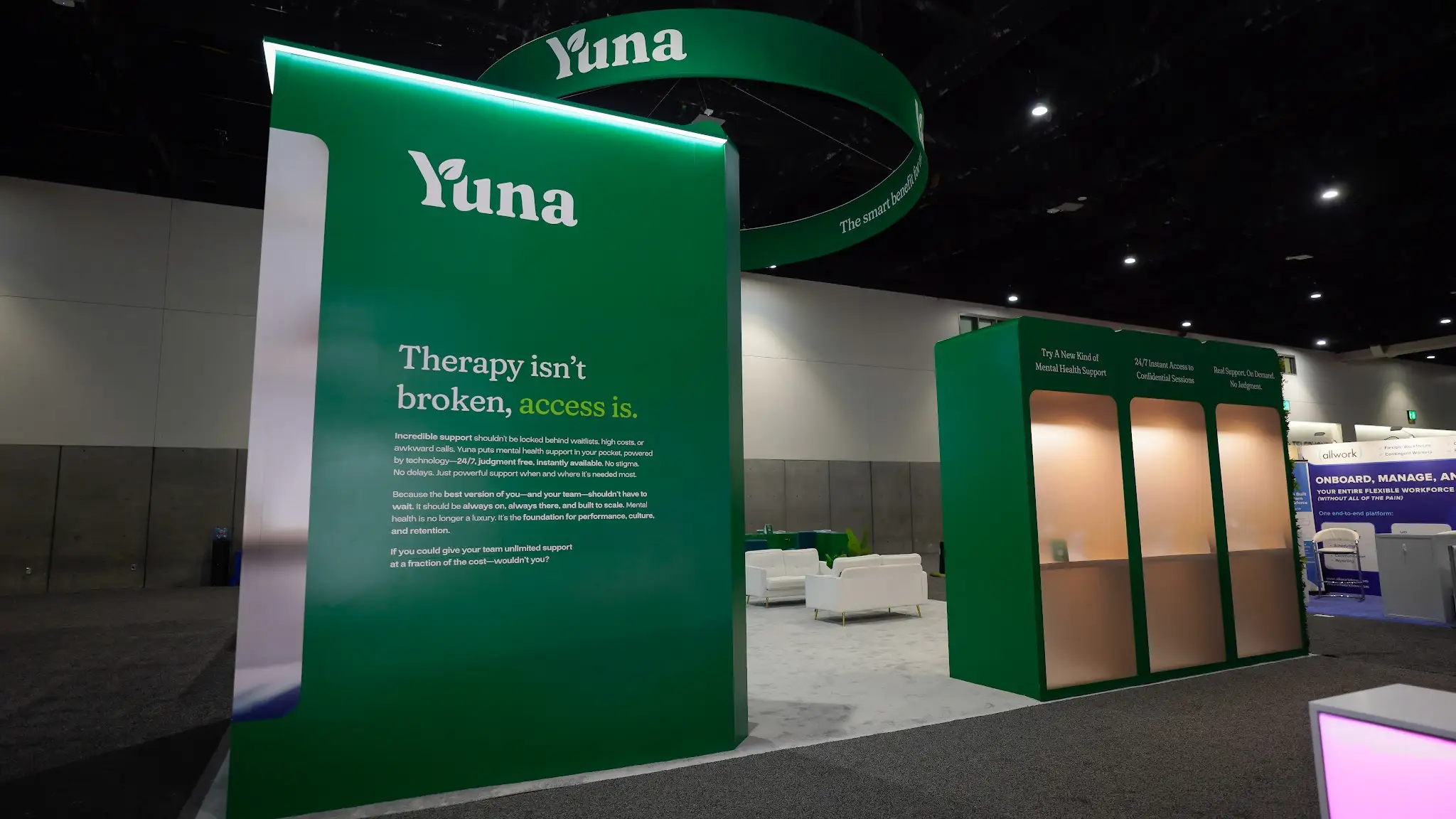 Yuna booth text wall close-up showing value proposition with three inset service panels including Try A New Kind of Mental Health Support, 24/7 Instant Access, and Real Support On Demand, with white lounge area visible