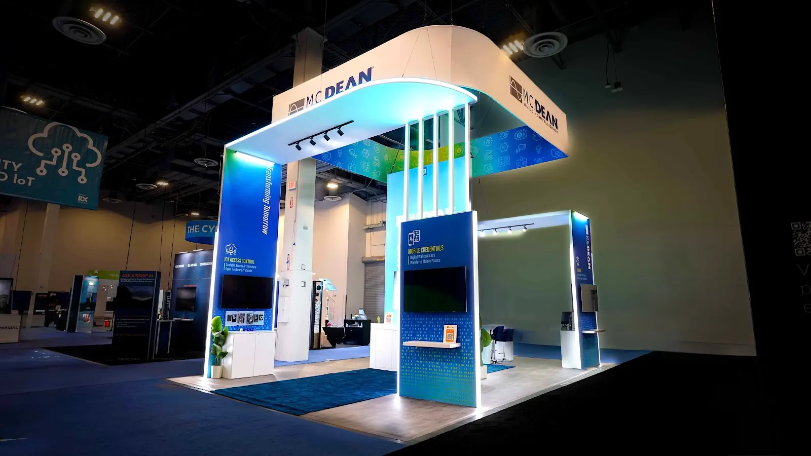 M.C. Dean booth rear-left exterior view showing floating canopy teal glow and Lifecycle Management kiosk tower at ISC West 2026