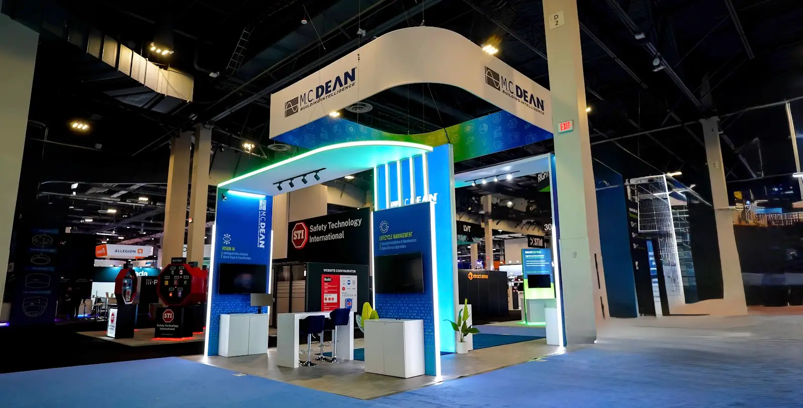 M.C. Dean 20x30 island exhibit full front-center view showing arched portal entry, Vision AI and IoT Access Control kiosk panels, STI partner display, and Build website configurator at ISC West 2026