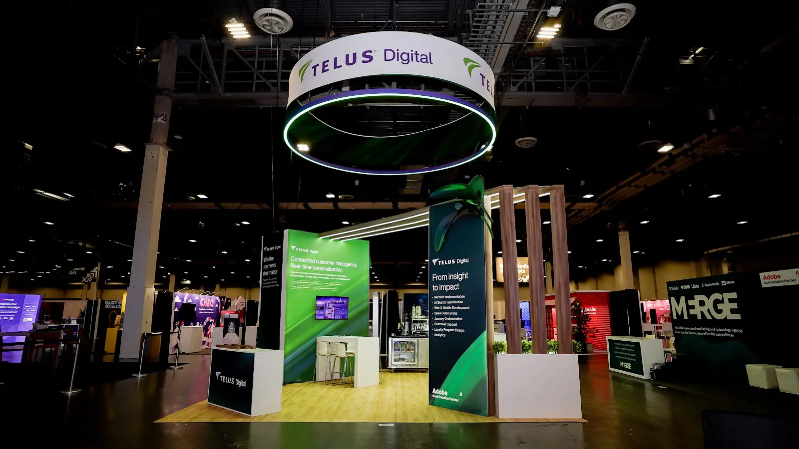 TELUS Digital booth front view showing vivid green Connected customer intelligence panel on left, dark From insight to impact navy tower on right with 3D leaf sculpture, and Adobe Gold Solution Partner badge at Adobe Summit 2026
