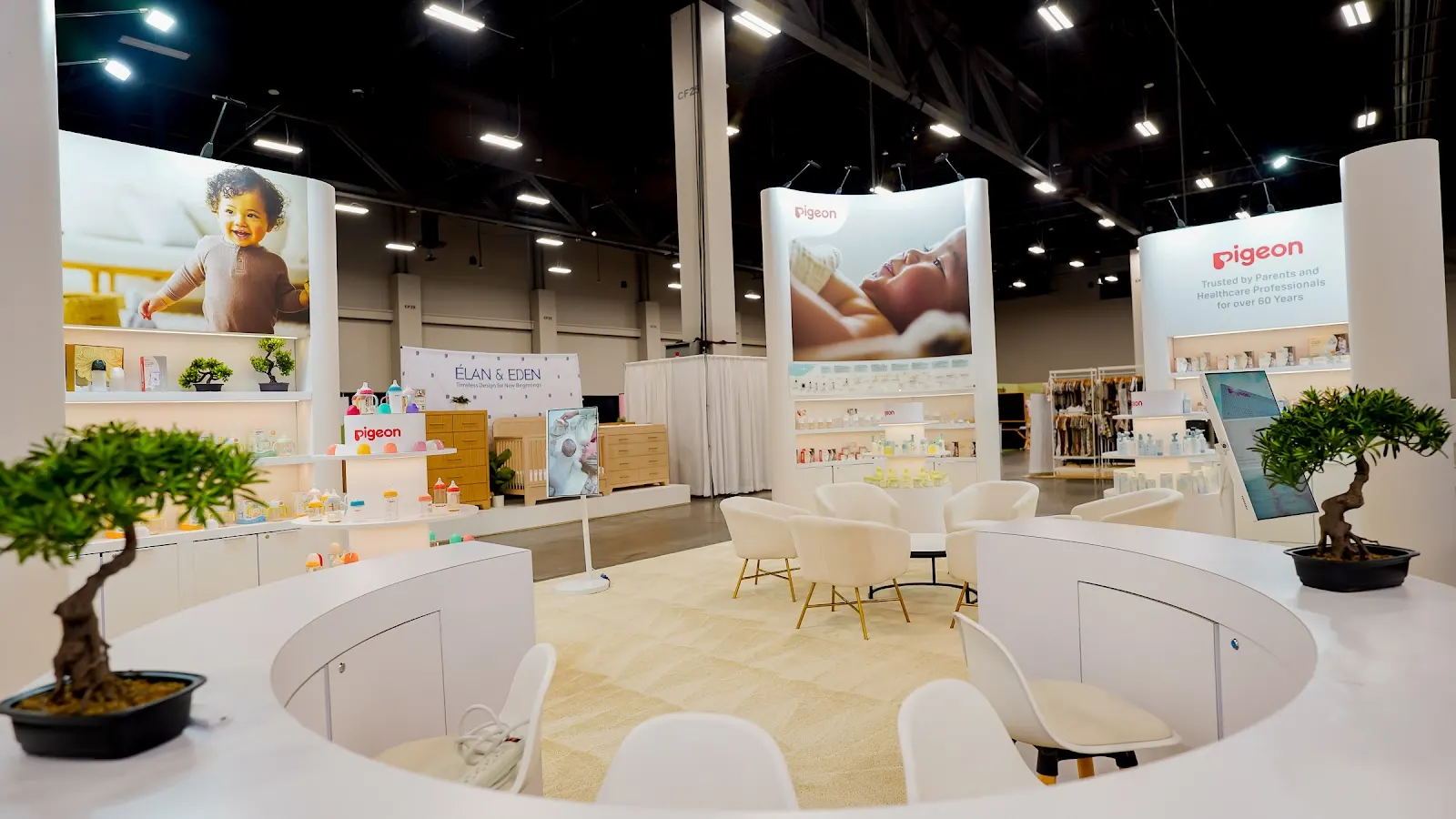 Wide-angle view of Pigeon baby products island booth at ABC Kids Expo 2026 showing full booth architecture with structured white product display walls, brand signage in Pigeon blue and white, organized product presentation across feeding, skincare and oral care categories, and visitors engaging with interactive demonstration areas