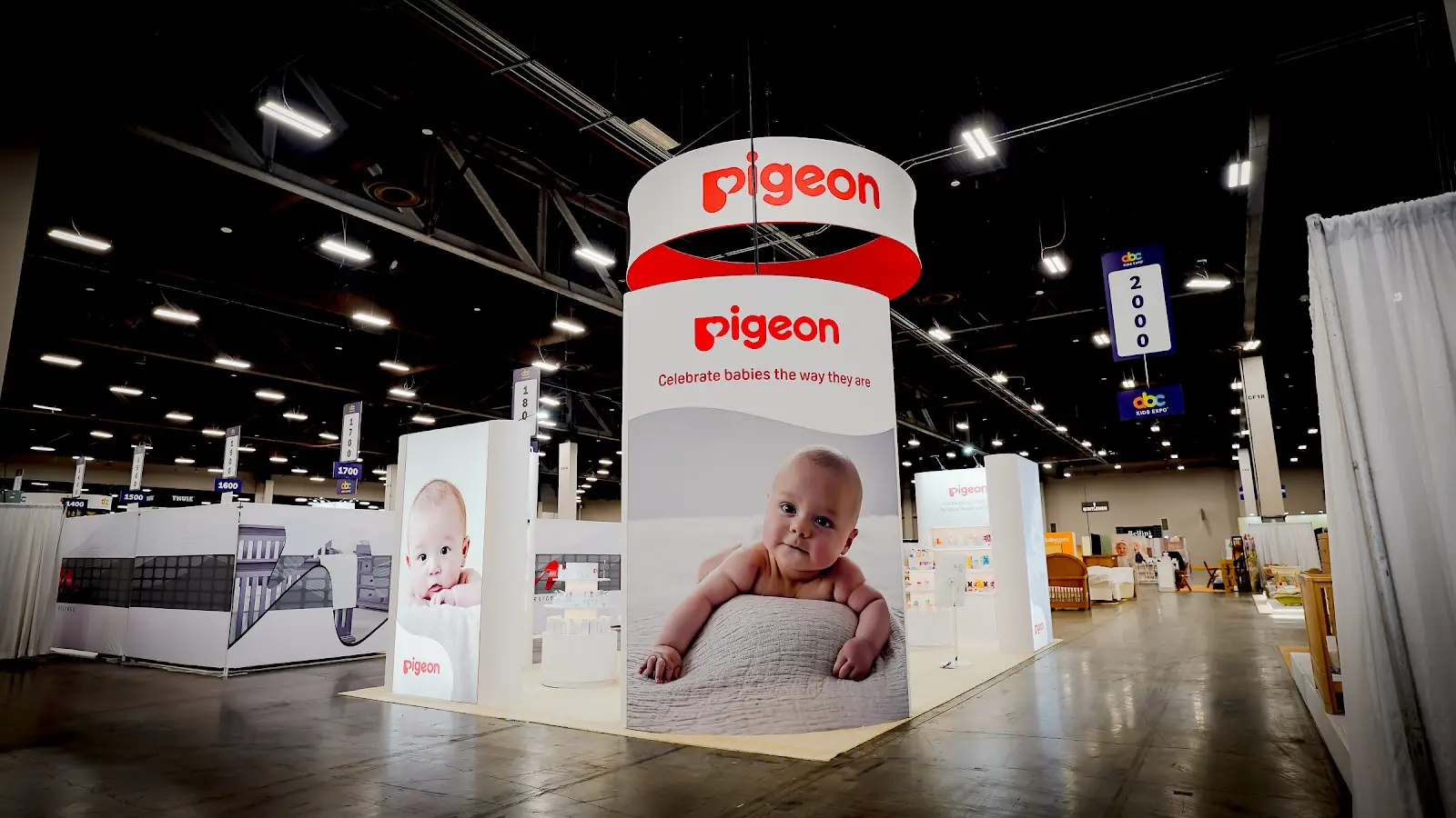 Detailed view of Pigeon baby products booth at ABC Kids Expo 2026 showing close-up of product display arrangement with feeding bottles, baby care items, and brand signage in the trademark Pigeon blue and white color palette under warm trade show lighting at Mandalay Bay Convention Center Las Vegas