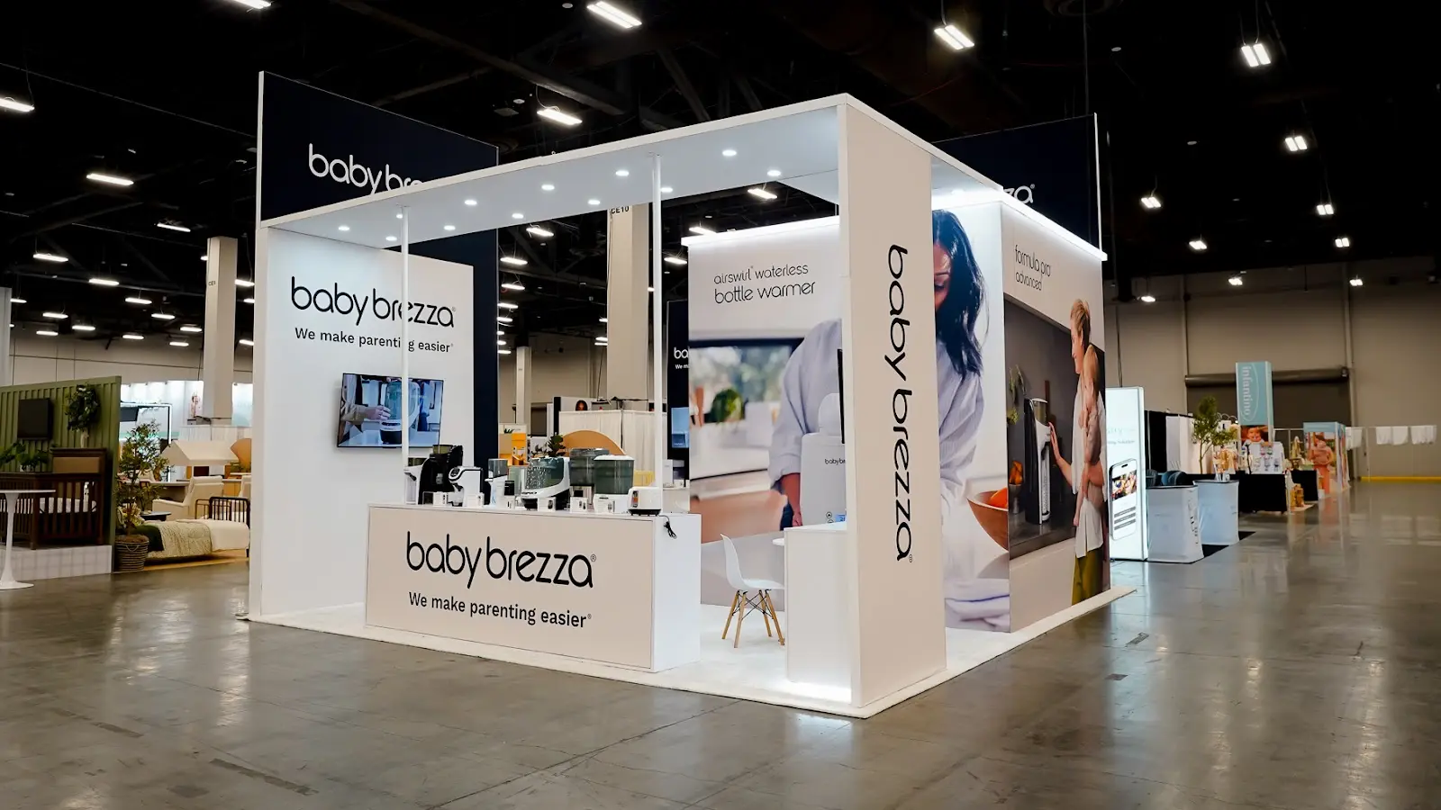 Modern white island exhibit for Baby Brezza at ABC Kids Expo 2026, laid out with product surfaces at counter height like a kitchen showroom