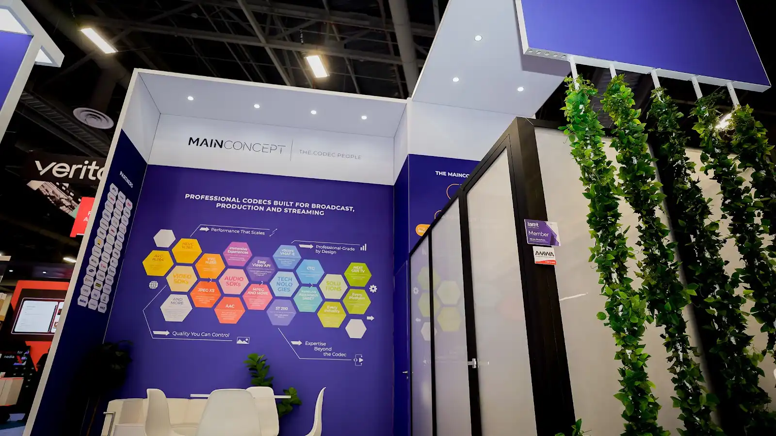 MainConcept purple trade show booth at NAB Show 2026 with dramatic hanging botanical vines suspended above the exhibit, creating an unexpected organic contrast against the technical codec software branding
