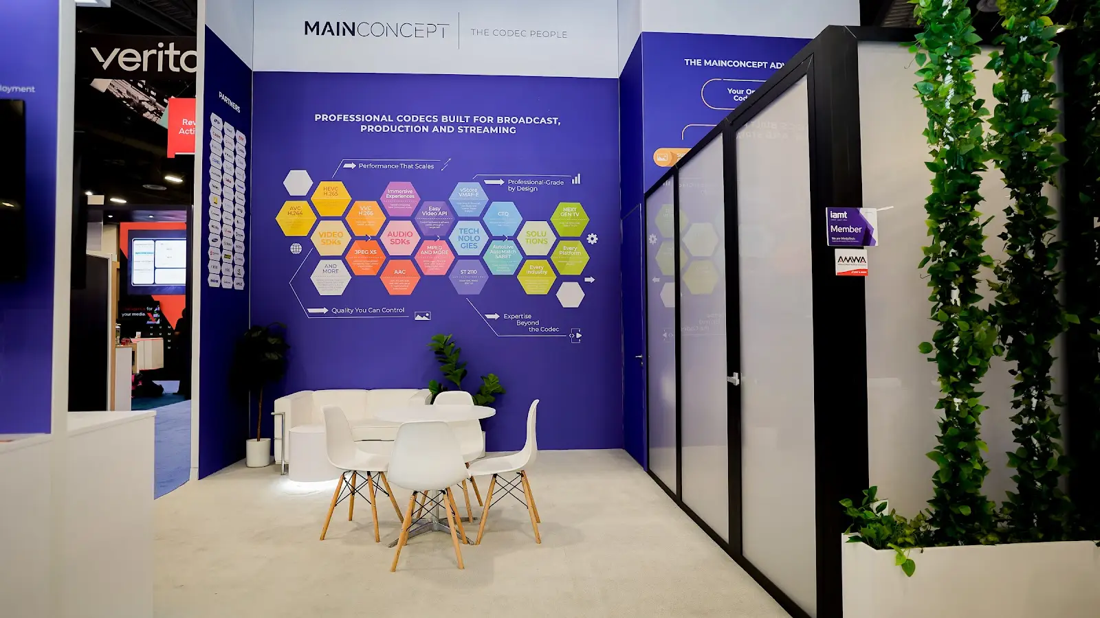 MainConcept purple trade show booth at NAB Show 2026 alternate angle showing deep violet paneling and branded surfaces standing out against the grey and black tech exhibits surrounding it on the convention floor