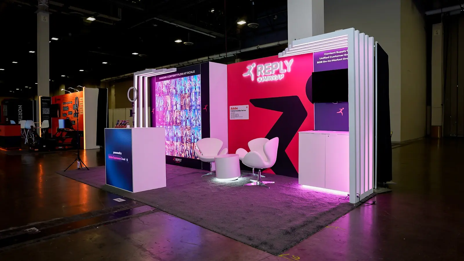 Close view of the pink LED panelling on the Comwrap Reply booth at Adobe Summit 2026, showing how the brand colour was built into the structure as a light source