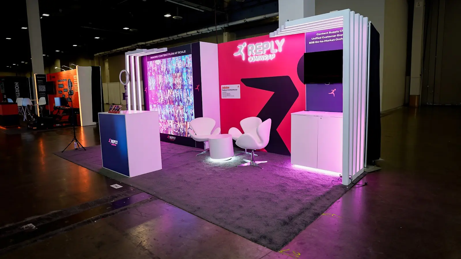 Full view of the Comwrap Reply custom exhibit at Adobe Summit 2026 in Las Vegas, showing the complete modern booth layout under show conditions