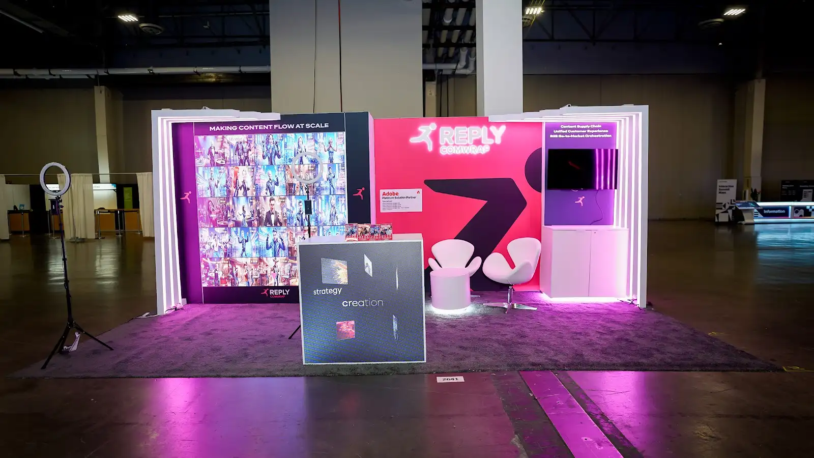 Comwrap Reply custom trade show booth at Adobe Summit 2026, front view showing the magenta and violet LED wall structure lit against the Venetian Expo show floor