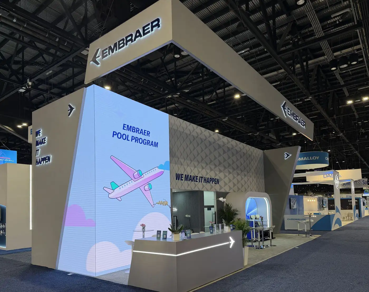 Corner of the Embraer booth at MRO Americas 2026 with Embraer Pool Program LED wall, We Make It Happen dimensional letters, and reception counter