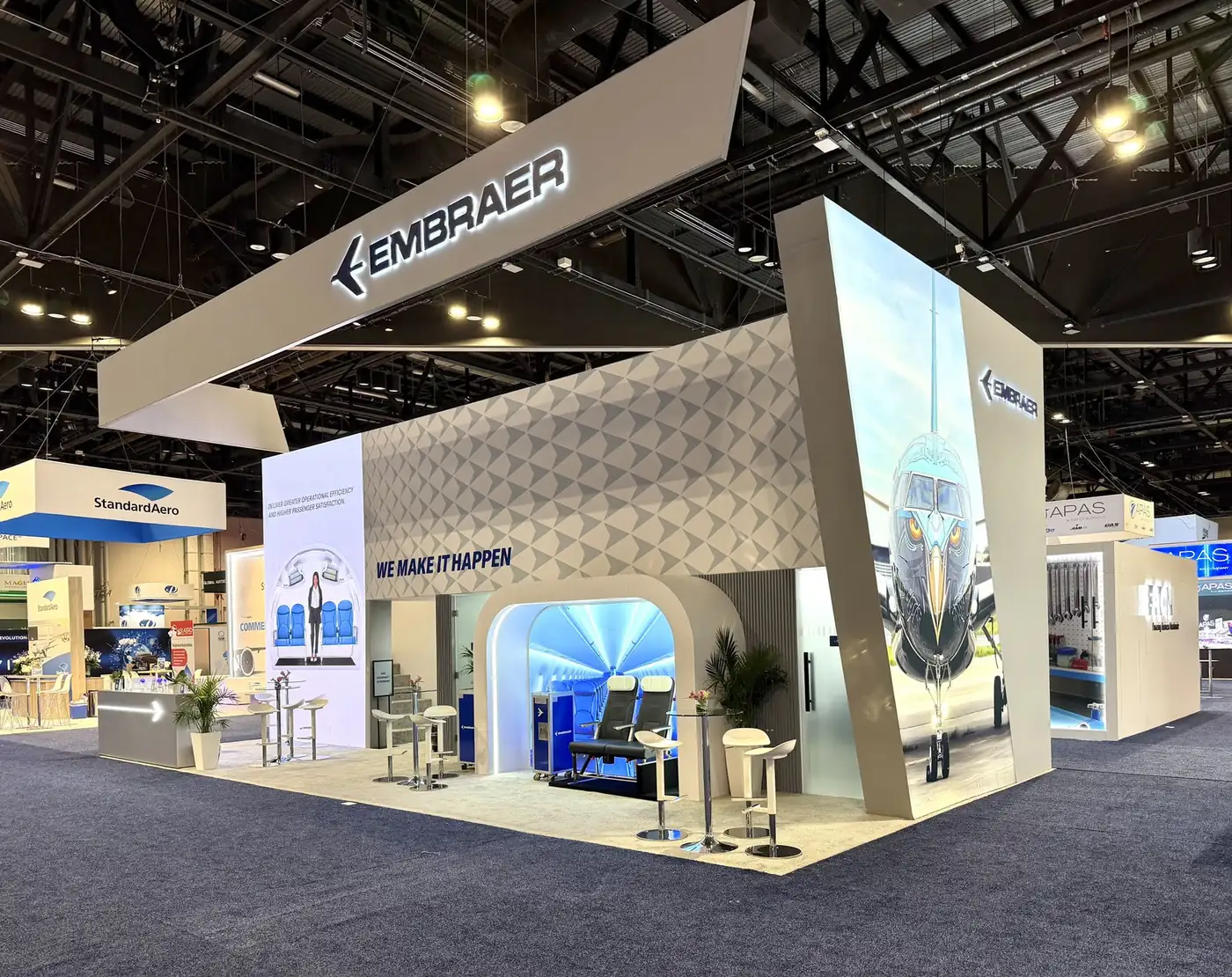 Three-quarter view of the Embraer double-deck booth at MRO Americas 2026 with the eagle-nose E-Jet graphic pillar and cabin mock-up entrance
