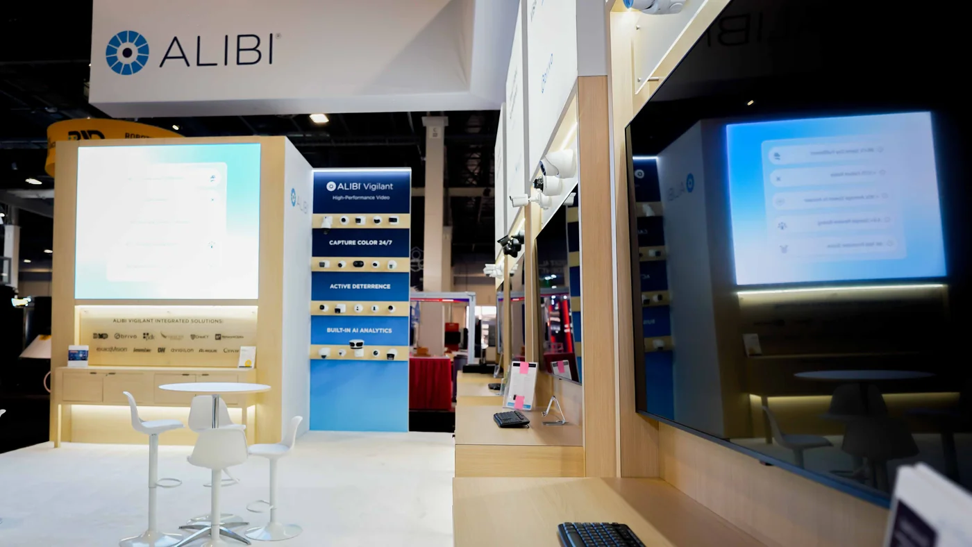 Interior detail of the Alibi Security booth at ISC West 2026 showing the Alibi Vigilant camera display tower with Capture Color 24/7, Active Deterrence and Built-in AI Analytics rows, the LED wall and demo counters