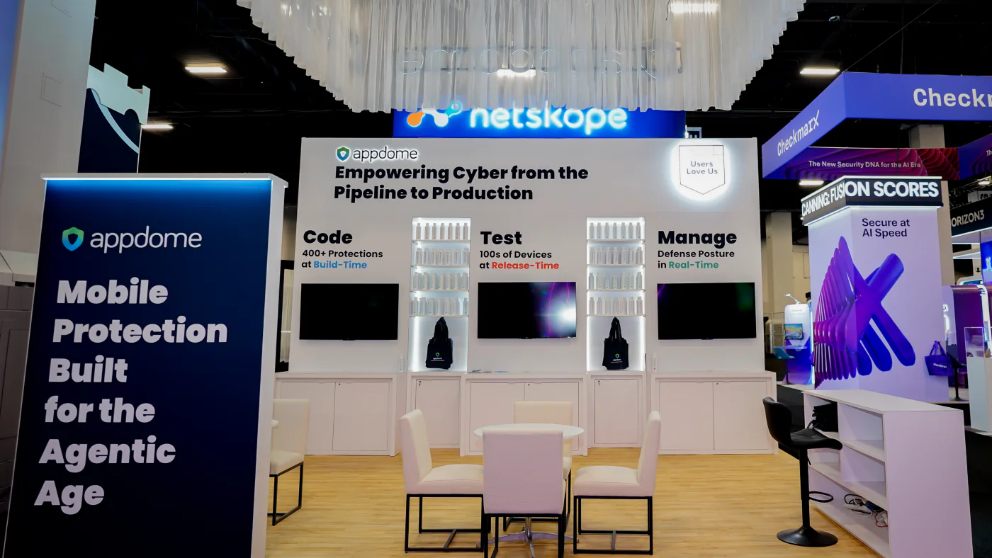 Appdome booth back wall at Black Hat USA 2026 with Code, Test and Manage panels, backlit product shelves, three screens and a white meeting table with chairs