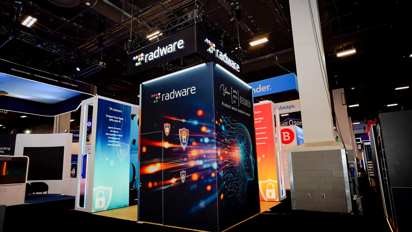 Corner view of the Radware booth tower at Black Hat USA 2026 with Your Apps APIs AI Secured headline, circuit-head graphic and hanging sign overhead