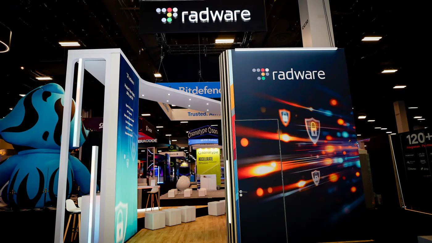 Radware booth at Black Hat USA 2026 with a shield-and-light-streak graphic wall, Protect Your Apps APIs and AI pillar and white cube seating on wood flooring