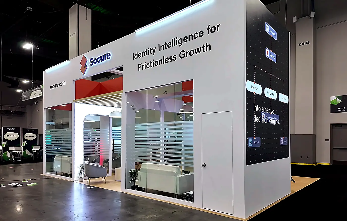 Angled view of the right side and back corner of the Socure 20x30 booth at Fintech Meetup 2026 with header graphics and slatted glass walls