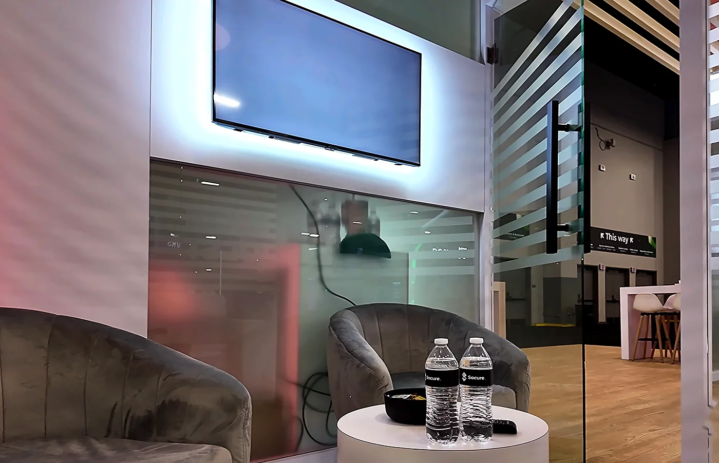 Lounge interior of the Socure 20x30 booth at Fintech Meetup 2026 with velvet armchairs, side table, wall-mounted monitor and slatted privacy screens