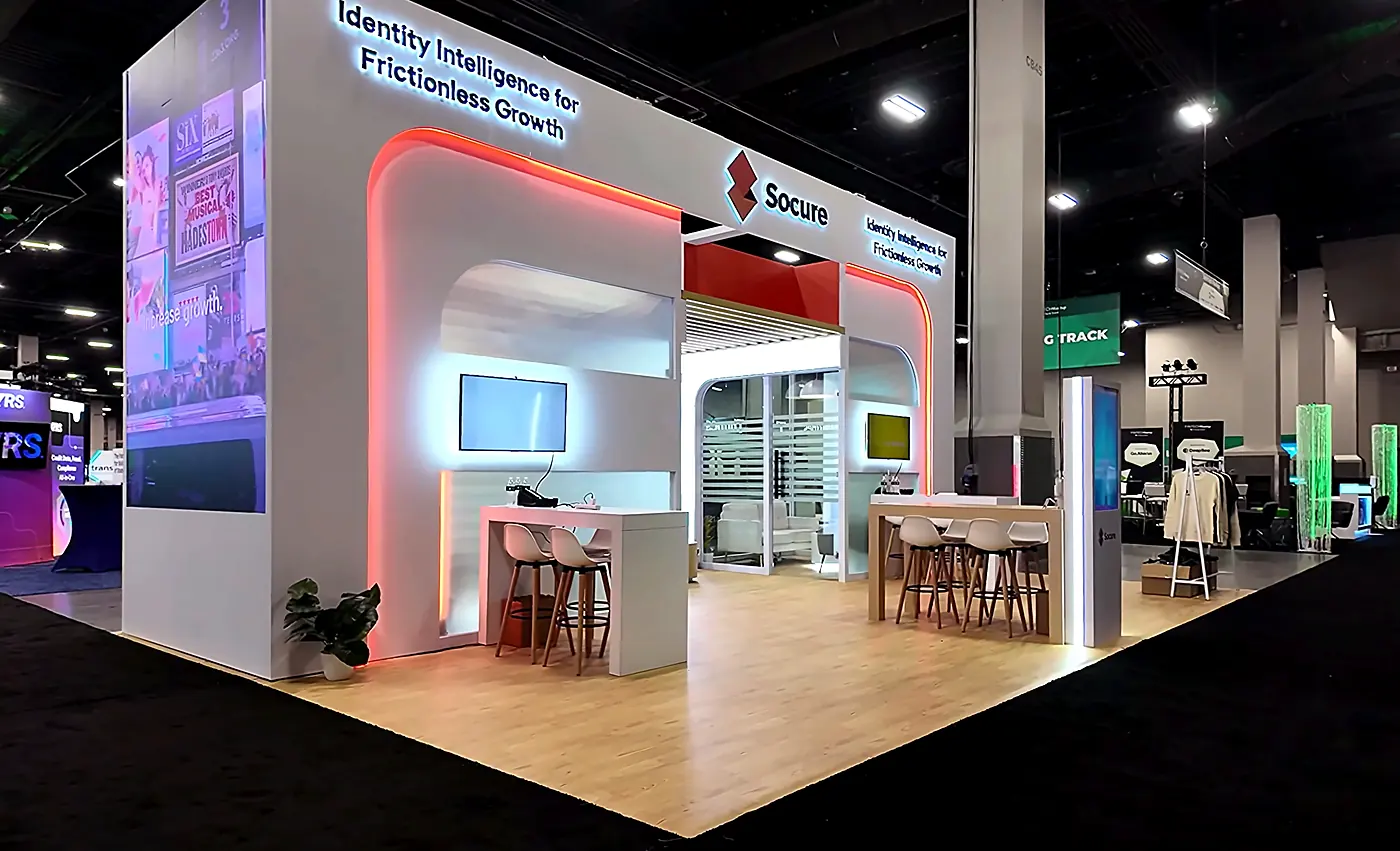 Socure 20x30 booth at Fintech Meetup 2026 seen from the left aisle with the arched entry, red LED accent, meeting counters and vertical graphic tower