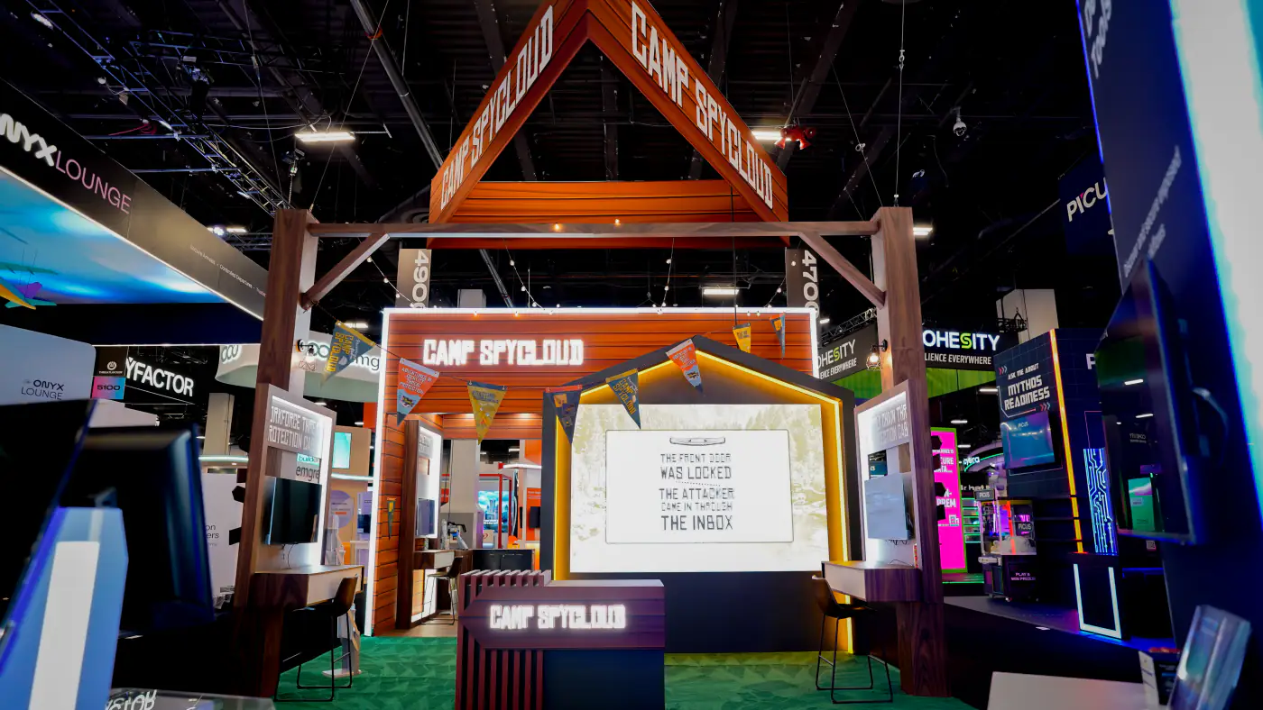A-frame lightbox demo stage at the Camp SpyCloud booth under pennant bunting, reading The front door was locked, the attacker came in through the inbox