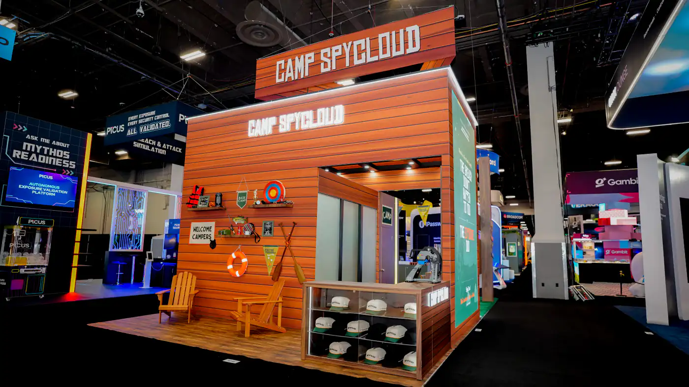 Front elevation of the Camp SpyCloud cabin with lit lettering, camp props, Adirondack chairs and a glass case of branded trucker hats
